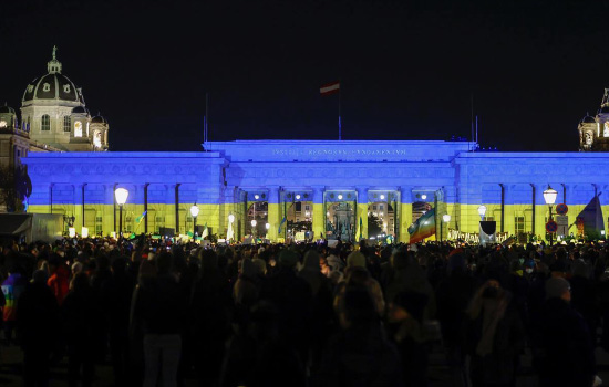 Nächtliches Heldentor in blaugelber Beleuchtung mit demonstrierten Menschen 