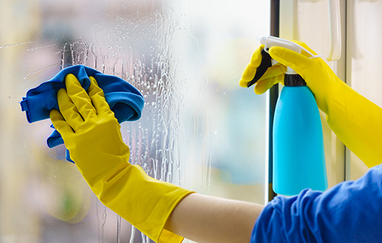 Weibliche Hand in gelben Handschuhen, die Fensterscheibe mit Lappen und Sprühwaschmittel reinigen. 