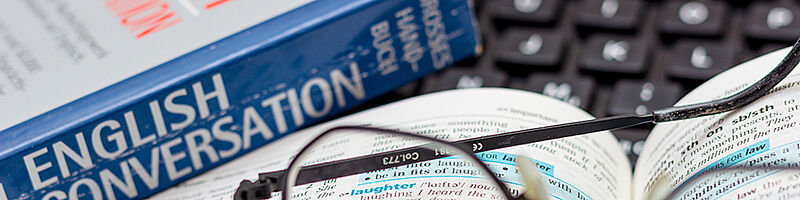 Brille liegt auf englisch Wörterbuch. Im Hintergrund ist eine Tastatur zu sehen.