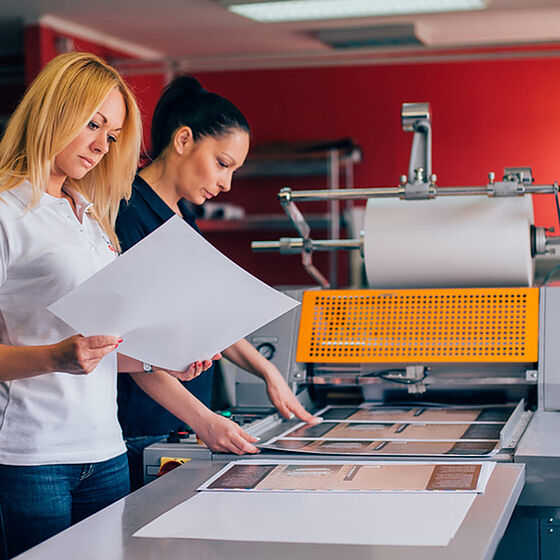 Two women look at print on a printing press