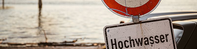 Hochwasser_Startseite_AdobeStock_321528897 Foto: Überschwemmtes Gebiet mit Schild "Achtung Hochwasser"