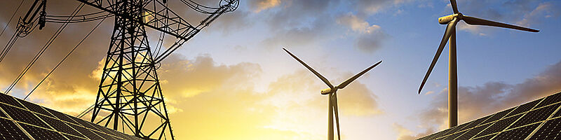 Ein Strommast, Windräder und eine Solaranlage bei blauem Himmel