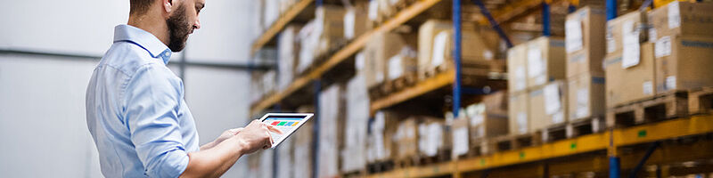 Lagersysteme_Fotolia_187312509_S Mann steht in Lagerhalle und macht eine Inventur