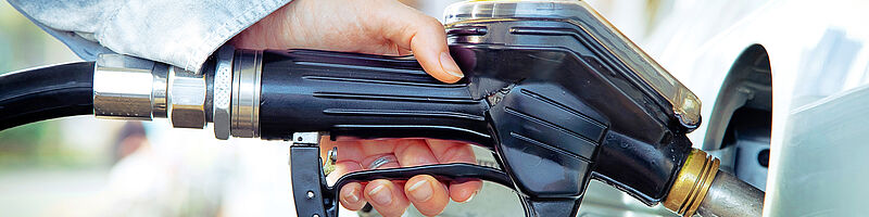 Eine Hand tankt ein Auto und steckt den Hahn in die Tanköffnung