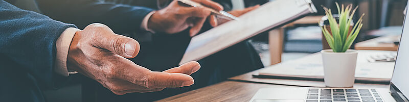 Beratungsdienstleistung_AdobeStock_251299510 Auf einem Tisch steht ein Laptop und zwei Männer sitzen davor und unterhalten sich