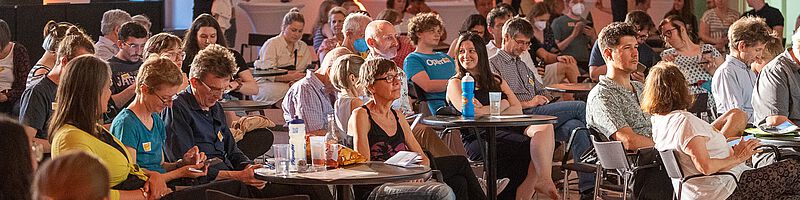 Das Publikum sitzt verteilt im Raum an kleinen runden Tischen