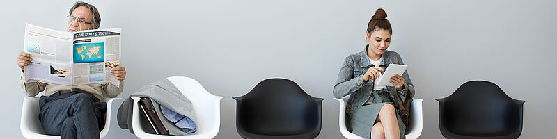 zwei Menschen die in einem Warteraum auf Stühlen sitzen