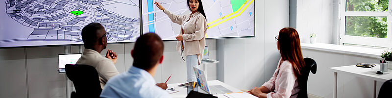 AdobeStock_964025304 Vier Menschen sind in einem Meeting und besprechen eine Raumordnung auf dem Bildschirm