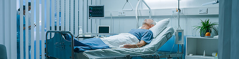 Mann an Monitor angeschlossen in einem Krankenhausbett