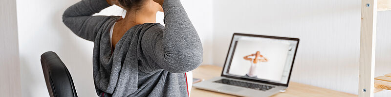 Frau sitzt vor Laptop und streckt sich