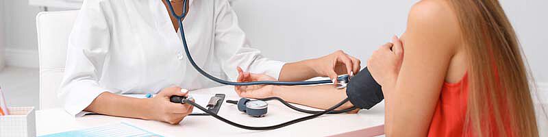 Ärztin misst bei Patientin Blutdruck mit Stethoskop